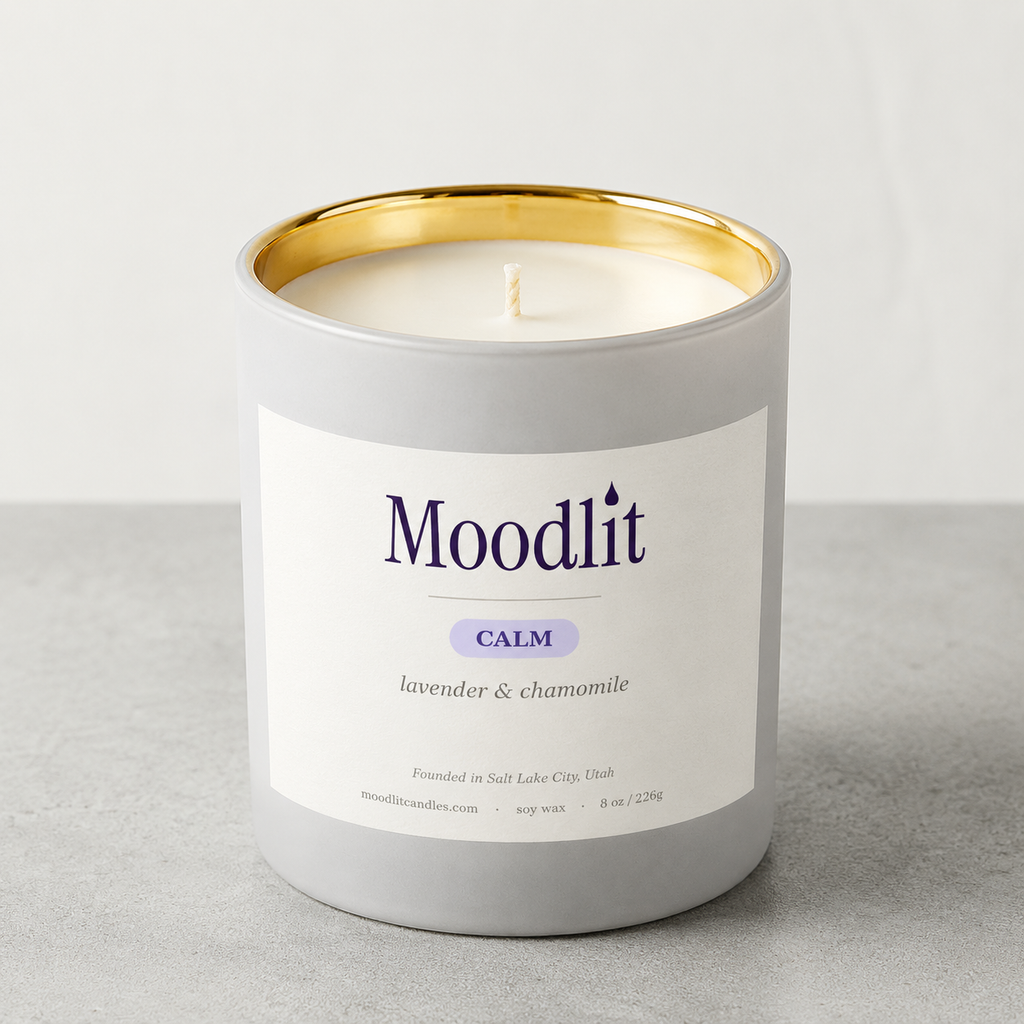 A Moodlit Calm soy wax candle in a matte gray jar with a gold inner rim and a white label featuring purple text, set against a neutral gray background.